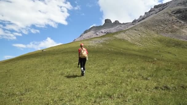한 소녀 사진작가가 구름이 있는 바위와 하늘을 배경으로 언덕 오르막길을 올라갑니다. 풍경 사진 작가를위한 개념 사진 투어 — 비디오