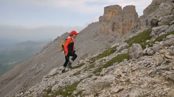 Niña fotógrafa sube la colina cuesta arriba contra el telón de fondo de acantilados de una meseta y el cielo con nubes. Concepto de foto tours para fotógrafos de paisajes — Vídeos de Stock