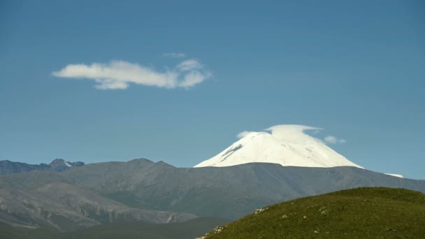 Středovýchodní krajina východního svahu hory ELBRUS. Formace v průzračném modrém nebi mraků nad zasněženou horou za letního slunného dne. Tvorba mraků změna počasí — Stock video
