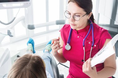 Dişçi ofisinde. Gözlüklü bir kadın diş hekimi genç bir kız hastanın çenebir döküm yapmaya hazırlanıyor. Bakım temiz ağız