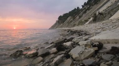 Yakın çekim yavaş hareket düşük geniş açı küçük deniz dalgaları kayalık bir plajda haddeleme. Sahil boyunca ileri ye doğru hareket edin. Sahil. Çakıl taşlı kayalık plajda akşam gün batımı