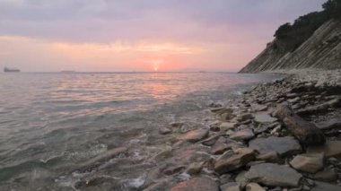 Yakın çekim yavaş hareket düşük geniş açı küçük deniz dalgaları kayalık bir plajda haddeleme. Sahil boyunca ileri ye doğru hareket edin. Sahil. Çakıl taşlı kayalık plajda akşam gün batımı