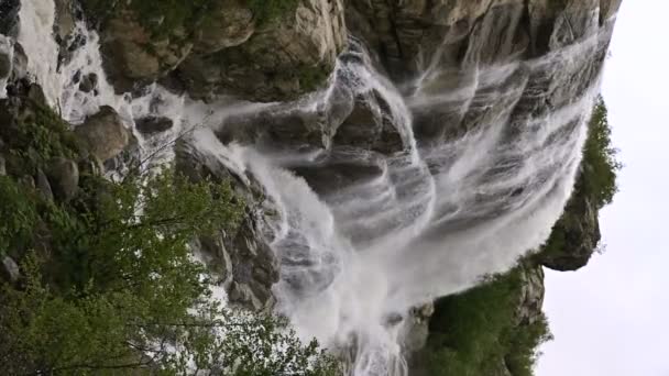 Vídeo vertical. Água em câmara lenta cai de uma rocha enorme. Cachoeira no ambiente natural em tempo nublado com chuva leve — Vídeo de Stock