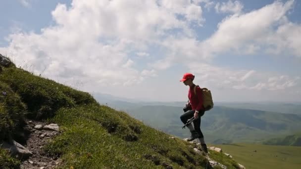 Dziewczyna fotograf idzie pod górę na tle i niebo z chmur w słoneczny dzień. Koncepcja Zdjęcia wycieczki dla fotografów krajobrazu. Trekking górski — Wideo stockowe