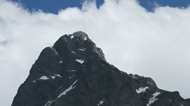 Κοντινό χρονικό διάστημα, απότομη απότομη βράχο με χιονισμένα έμπλαστρα σε φόντο στροβιλίζονται πυκνά σύννεφα σε μια ηλιόλουστη μέρα. Έννοια αλλαγής καιρού βουνού — Αρχείο Βίντεο
