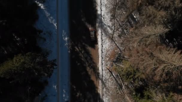 Widok z lotu ptaka nieznanego samochodu terenowego jazdy wzdłuż asfaltowej drogi w lesie iglastym zimą w słoneczny dzień. Koncepcja transportu zimą. Niski klucz — Wideo stockowe