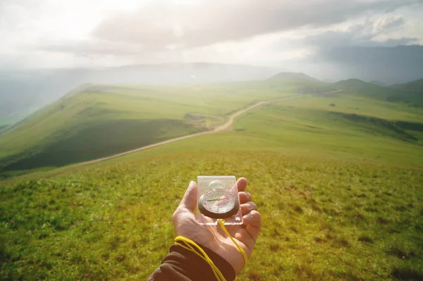 Male hand with a magnetic compass ea against the backdrop of a beautiful landscape at sunset. The concept of navigating the search for your own path and orientation to the cardinal points — Stock Photo, Image