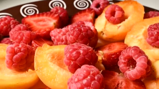 Närbild av skivade röda jordgubbar och hallon bredvid aprikoser på en tallrik. Live-kamera. Begreppet läcker och hälsosam kost och vegetarianism. — Stockvideo