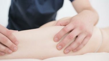 Yakın çekim bir erkek fizyoterapist pamuk bir delikanlı yanında profesyonel bir spa salonunda genç bir kadının kalça ve kalça ısınmak için hafif bir masaj yapıyor. 4k masaj vücut bakım konsepti