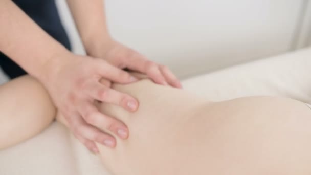 Närbild av en manlig sjukgymnast gör en lätt massage för att värma upp höfter och skinkor av en ung kvinna i en professionell Spa salong bredvid en kvist bomull. 4K massage kroppsvård koncept — Stockvideo