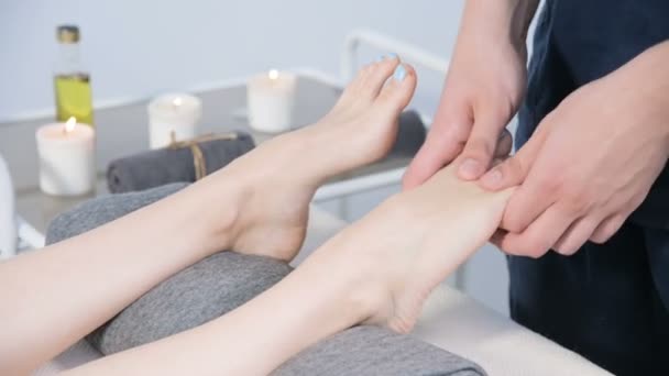 一名男性理疗师在美容和健康水疗中心为年轻女孩做足部按摩的特写镜头。足部和身体护理概念 — 图库视频影像