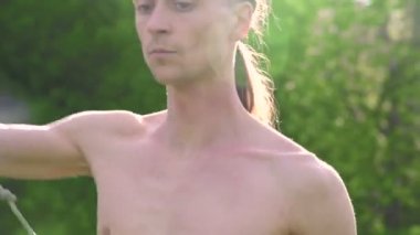 Orta uzun saçlı ve çıplak gövdeile genç bir adam dövüş sanatı eğitimli ve bir yaz sabahı rotasyon açık havada bir personel veya yük halat ile konuşmadan önce vurdu. Düşük açı