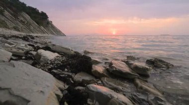 Yakın çekim yavaş hareket düşük geniş açı küçük deniz dalgaları kayalık bir plajda haddeleme. Sahil boyunca ileri ye doğru hareket edin. Sahil. Çakıl taşlı kayalık plajda akşam gün batımı