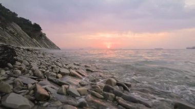 Yakın çekim yavaş hareket düşük geniş açı küçük deniz dalgaları kayalık bir plajda haddeleme. Sahil boyunca ileri ye doğru hareket edin. Sahil. Çakıl taşlı kayalık plajda akşam gün batımı