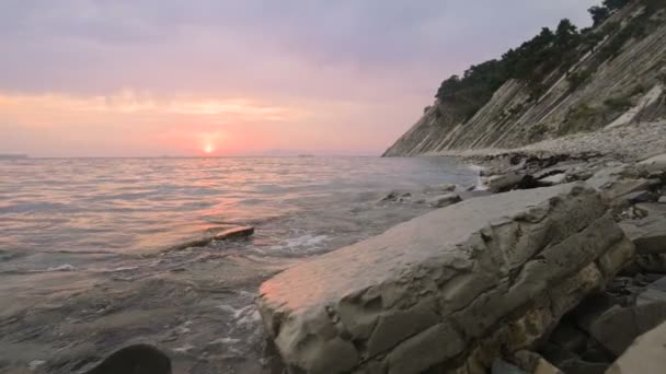 Primer plano cámara lenta bajo gran angular pequeñas olas marinas rodando en una playa rocosa. Movimiento a lo largo de la playa adelante. Junto al mar. Atardecer en una playa rocosa de guijarros — Vídeos de Stock