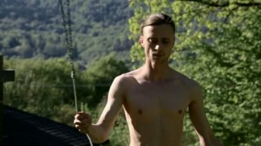 Bir yangın gösterisi için uzun saçlı bir adamın orta yakın çekim sabah eğitimi. Açık havada güneşli bir yaz sabahı meşaleler ve zincirler ile ateş olmadan bir performans için hazırlık