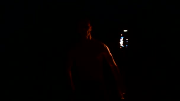 Крупный план Медленное движение молодого человека в черных штанах в полной темноте показывает представление вращающегося горящего факела. Медитация в движении. Спокойно и непоколебимо. Работа с огнем. Низкий ключ — стоковое видео