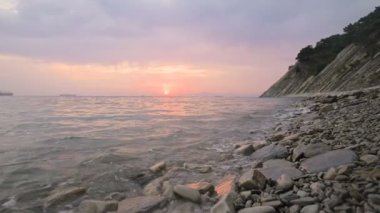 Yakın çekim yavaş hareket düşük geniş açı küçük deniz dalgaları kayalık bir plajda haddeleme. Sahil boyunca ileri ye doğru hareket edin. Sahil. Çakıl taşlı kayalık plajda akşam gün batımı