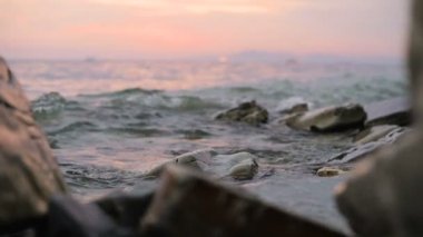 Yakın çekim yavaş çekim düşük açı küçük deniz dalgaları kayalık bir plajda haddeleme. Sahil. Çakıl taşlı kayalık plajda akşam gün batımı