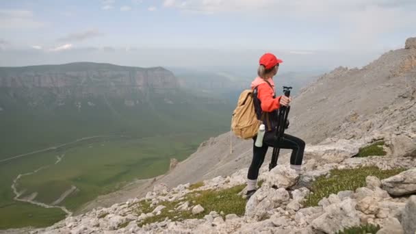 Dívčí fotograf stojí na svahu od stoupání na úbočí kopce a na pozadí skalní plošiny a nebe s mraky. Konceptuální výlety fotografií na krajinářské fotografy — Stock video
