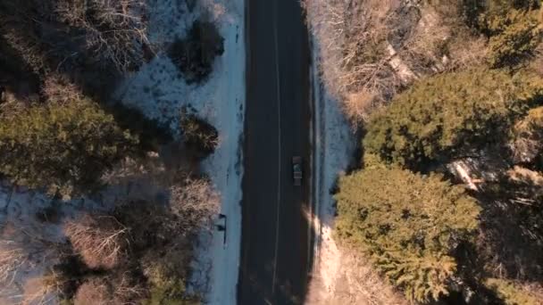 Vue aérienne d'une voiture hors route inconnue circulant le long d'une route asphaltée dans une forêt de conifères en hiver par une journée ensoleillée. Concept de transport hivernal. Clé basse 