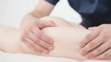 Yakın çekim bir erkek fizyoterapist pamuk bir delikanlı yanında profesyonel bir spa salonunda genç bir kadının kalça ve kalça ısınmak için hafif bir masaj yapıyor. 4k masaj vücut bakım konsepti