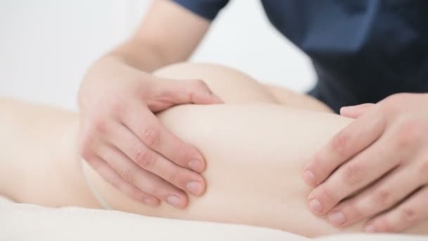 Nahaufnahme eines männlichen Physiotherapeuten, der in einem professionellen Wellness-Salon neben einem Zweig Baumwolle eine leichte Massage zum Aufwärmen der Hüften und des Gesäßes einer jungen Frau durchführt. 4k Massage Körperpflege-Konzept — Stockvideo