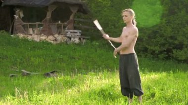 Bir gösteri için uzun saçlı bir adamın Orta Yakın Çekim Sabah eğitimi. Yeşil bir ormanın yanında açık havada güneşli bir yaz sabahı meşaleler ve zincirler ile ateş olmadan bir performans için hazırlık.