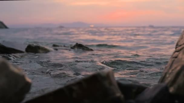 Primer plano cámara lenta ángulo bajo pequeñas olas marinas rodando en una playa rocosa. Junto al mar. Atardecer en una playa rocosa de guijarros — Vídeo de stock