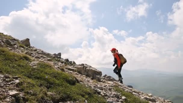 Dziewczyna fotograf idzie pod górę na tle i niebo z chmur w słoneczny dzień. Koncepcja Zdjęcia wycieczki dla fotografów krajobrazu. Trekking górski — Wideo stockowe