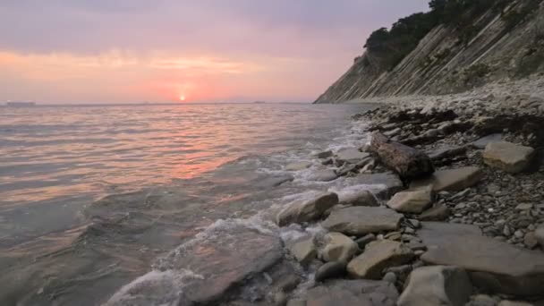 Primer plano cámara lenta bajo gran angular pequeñas olas marinas rodando en una playa rocosa. Movimiento a lo largo de la playa adelante. Junto al mar. Atardecer en una playa rocosa de guijarros — Vídeo de stock