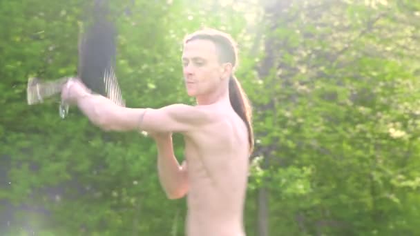 Medium shot A young man with long hair and a naked torso is trained in martial art and before speaking with a staff or load rope in rotation outdoors on a summer morning. Low angle — Stock Video