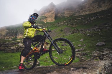 Yan görüş geniş açı kısmen bir dağ bisikleti bir adam bulutlu gökyüzü ve epik kayaların arka plan karşı kayalık arazi üzerinde seyahat. Bir dağ bisikleti ve mtb yokuş aşağı kavramı