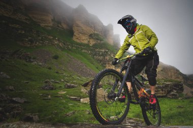 Yan görüş geniş açı kısmen bir dağ bisikleti bir adam bulutlu gökyüzü ve epik kayaların arka plan karşı kayalık arazi üzerinde seyahat. Bir dağ bisikleti ve mtb yokuş aşağı kavramı