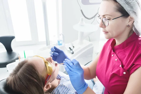 歯科医院で眼鏡をかけた女性歯科医が、若い女の子の患者の顎のキャストを作る準備をしています。ケアクリーンな口 — ストック写真