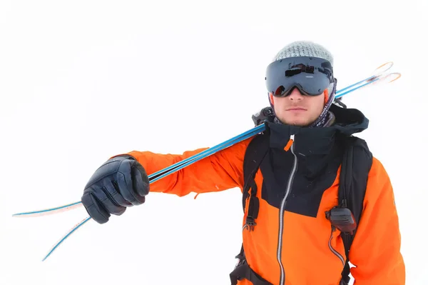 Profesionální lyžař v oranžovém černém obleku s černou lyžařskou maskou se lyží v dlaních stojí s nevelkou hmotností během sněhové bouře na světle pozadí ve sněhu — Stock fotografie