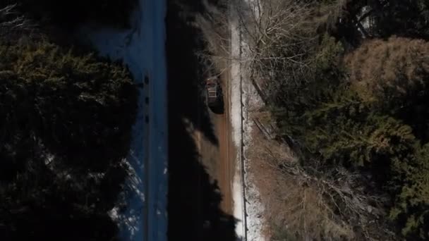 Vista aérea de un desconocido todoterreno conduciendo a lo largo de una carretera asfaltada en un bosque invernal de coníferas en un día soleado. Concepto de transporte de invierno. Tecla baja — Vídeo de stock