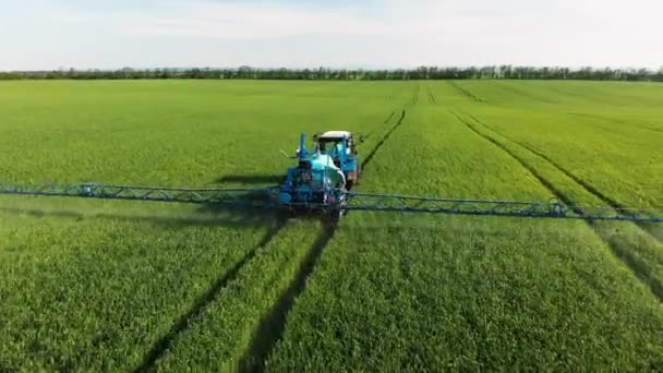 Вид с воздуха на трактор, который поливает зеленое поле специальной установкой. Процесс разбрызгивания поля пестицидами и защита от насекомых грызунов, паразитов и вредителей . — стоковое видео