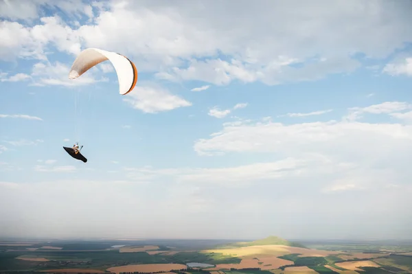 A white-orange paraglider flies over the mountainous terrain — Stock Photo, Image