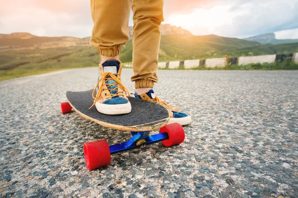 Güneş batımında asfalt arka planda bir Longboard üzerinde bez spor ayakkabıları erkek bacaklar yakın çekim. Erkek bacakları olan büyük bir kaykay. Gençlik eğlence konsepti — Stok fotoğraf