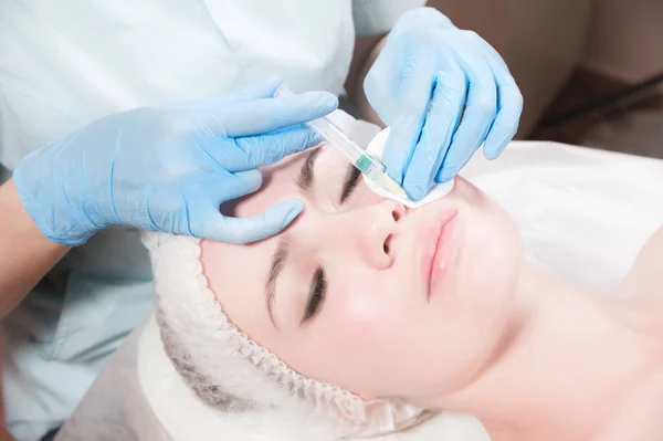 Close-up Jovem atraente recebe injeções faciais anti-envelhecimento. Ela se deita calmamente em uma clínica ou salão. Um jovem cosmetologista experiente enche rugas femininas com ácido hialurônico de uma seringa — Fotografia de Stock