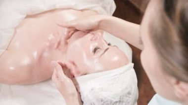 Girl beautician in a mask and gloves makes a salubrious facial massage to an attractive woman. New generation cosmetology massage