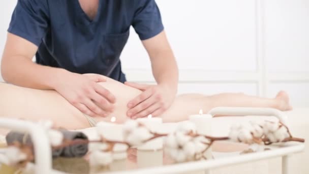 Nahaufnahme einer Kerze auf einem Massagetisch mit einem Baumwollzweig vor dem Hintergrund eines männlichen Physiotherapeuten, der eine entschärfte Massage durchführt. 4k Massage Körperpflege-Konzept — Stockvideo