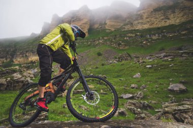 Yan görüş geniş açı kısmen bir dağ bisikleti bir adam bulutlu gökyüzü ve epik kayaların arka plan karşı kayalık arazi üzerinde seyahat. Bir dağ bisikleti ve mtb yokuş aşağı kavramı