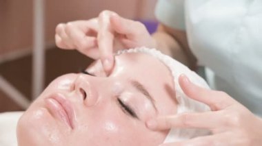 Kapalı Spa yüz masajı. Profesyonel masaj terapisti çekici bir spa salonu müşterisine yüz masajı yapıyor.