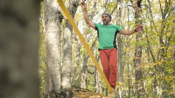A Slack man aged with a beard in sportswear walks balancing on the slackline. The concept of sports activity at the age of 50 — Stock Video
