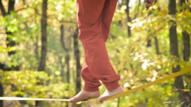 A Slack man aged with a beard in sportswear walks balancing on the slackline. The concept of sports activity at the age of 50. Athletes foot closeup — ストック動画