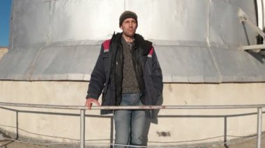 Yetişkin bir erkek gözlemevi çalışanı gözlem kubbesinin gözlem güvertesinde duruyor ve uzaklığa bakıyor. Açık mavi gökyüzüne karşı havadan görüş. Astronomi bilim konsepti