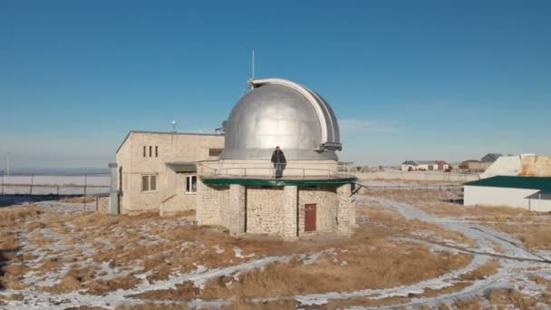 Een volwassen mannelijke observatoriummedewerker staat op het observatiedek van de observatiekoepel en kijkt in de verte. Luchtzicht tegen een helderblauwe lucht. Astronomiewetenschapsconcept — Stockvideo