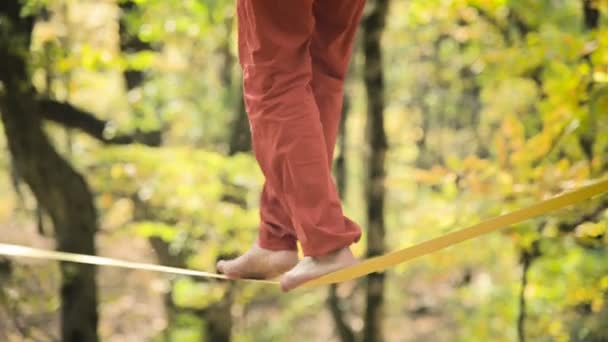 Un hombre de Slack envejecido con barba en ropa deportiva camina balanceándose en el slackline. El concepto de actividad deportiva a la edad de 50 años. Primer plano del pie de los atletas — Vídeos de Stock